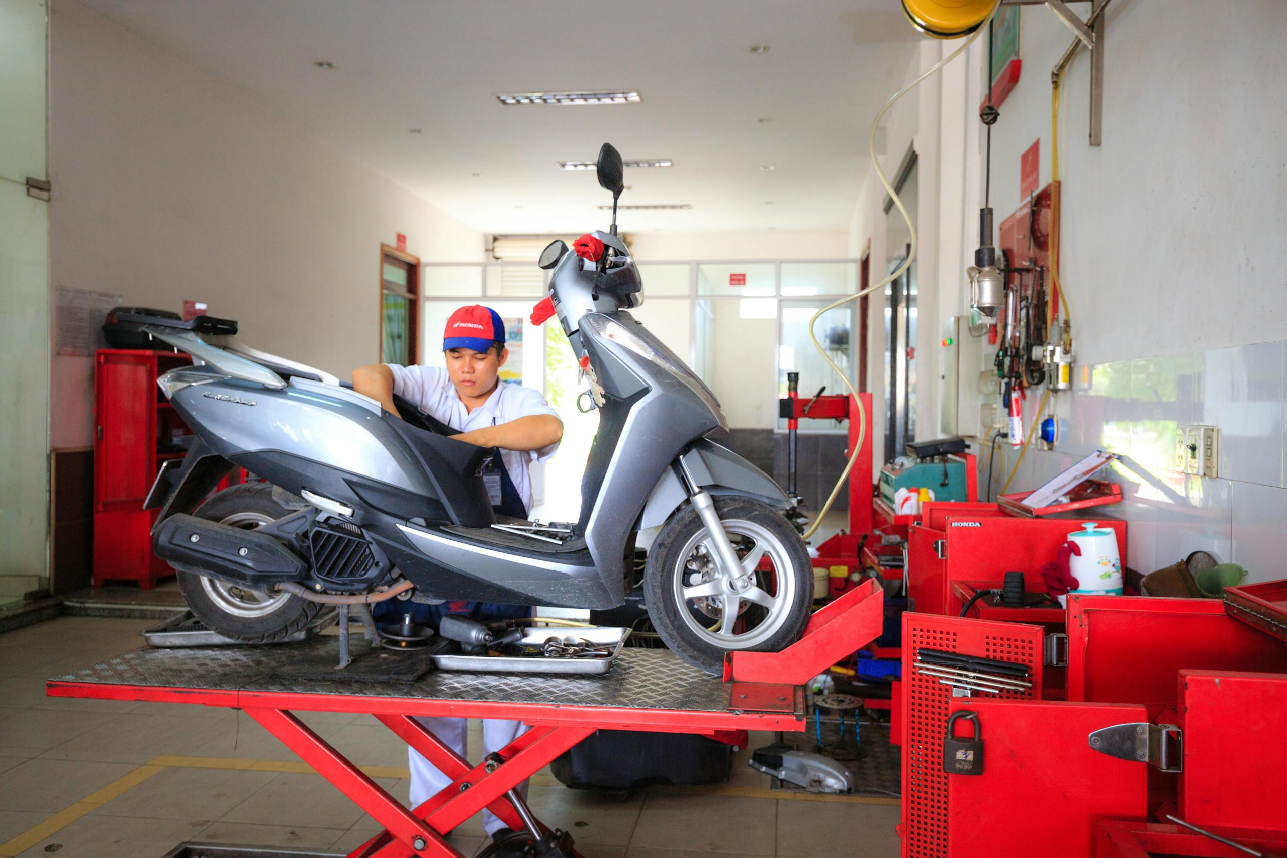 Mechanic performing maintenance on a scooter in an indoor repair shop setting.